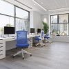 mesh office chair with blue mesh back and fabric seat in office roomset. With white office desks and city view