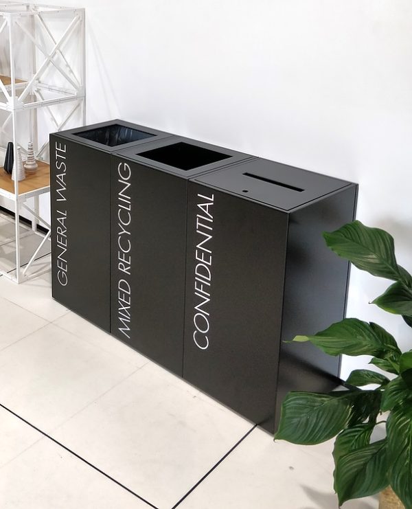 row of black office recycling bins. i confidential with slot and lock and 2 standard with white lettering for waste streams