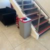 office recycling bin with silver body and red top at bottom of stairs