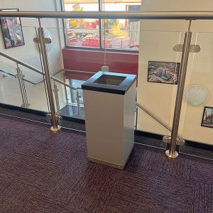 office recycling bin with silver body and black top in room shot at top of stairs