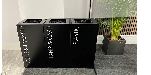 row of three black office recycling bins with white lettering general waste, paper and card and plastic