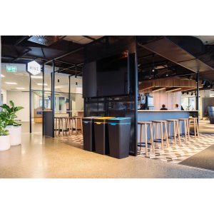 bar area with 3 black office recycling bins with coloured lids for different waste stream