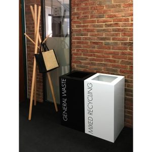 black office recycling bin with white General Waste lettering and white office recycling bin with Mixed Recycling black lettering. in an office by coat stand