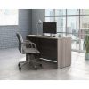 office desk with panel end legs in attractive elm finish. In office setting with office chair and city view